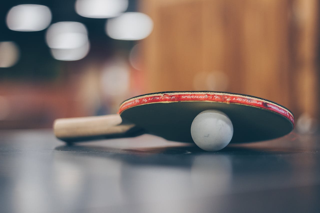 expertise-01 Close-up of a ping pong paddle and ball on a table with an artistic bokeh background, indoors.